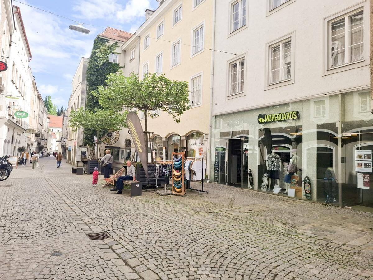 Belebtes Stadtbild mit Geschäften, Kopfsteinpflaster und Passanten, typisch für eine Innenstadtlage.