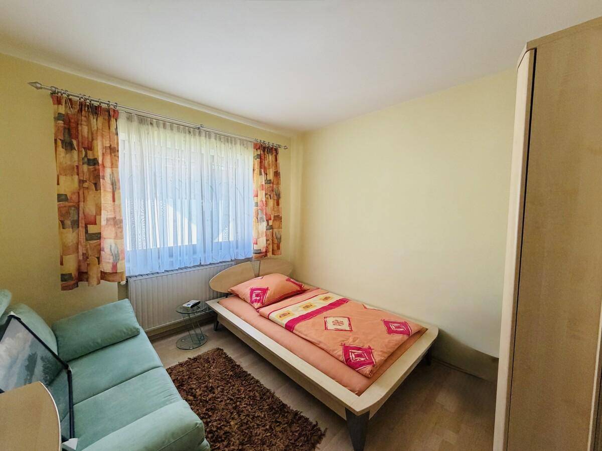 Kleines Schlafzimmer mit Einzelbett, Sofa und Fenster mit Blick ins Grüne.