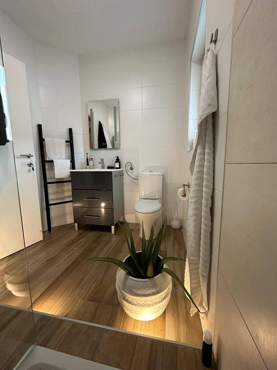 Helles Badezimmer mit modernem Waschtisch, WC und ebenerdiger Dusche, gut beleuchtet.
