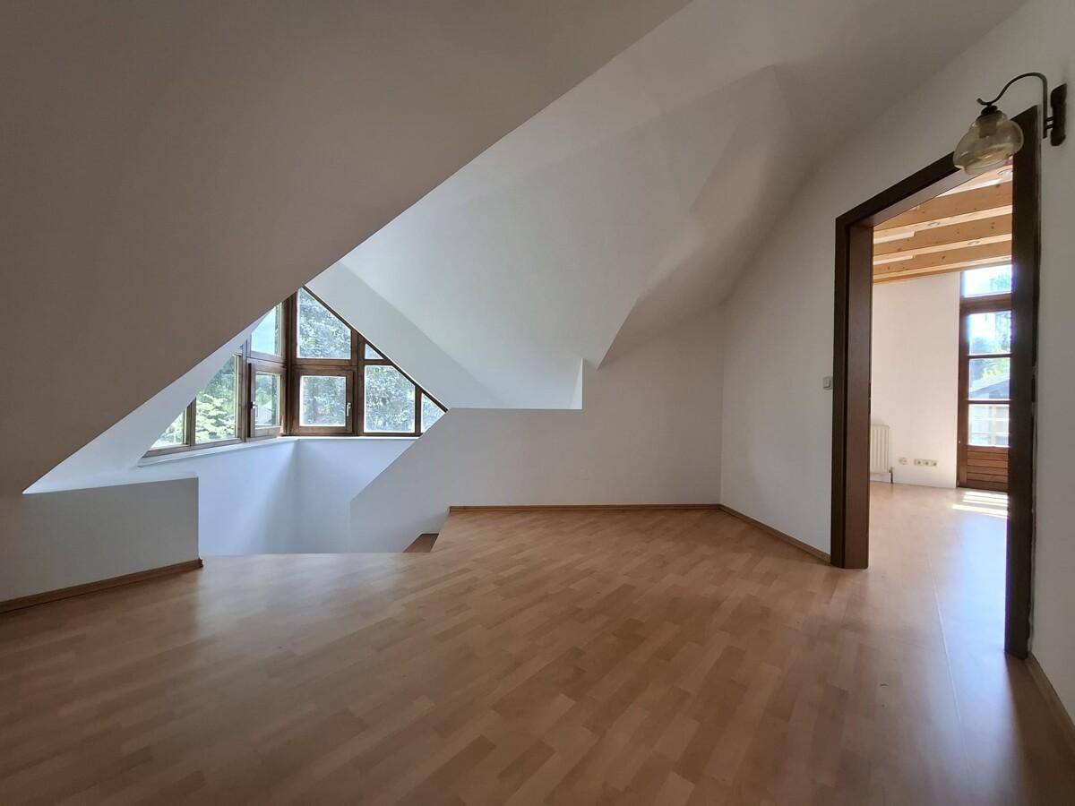Geräumiger Dachbodenraum mit Holzparkettboden, schrägen Wänden und Fenstern.