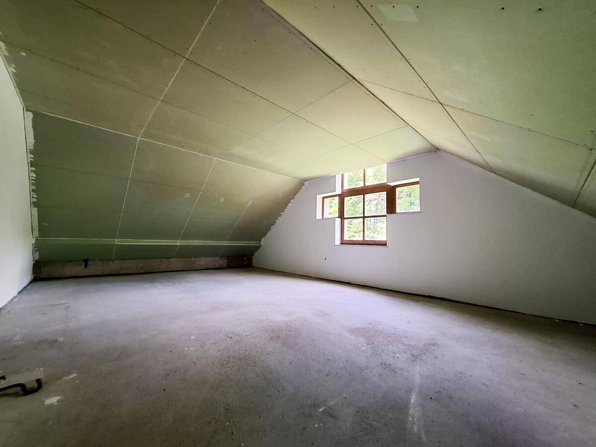 Unausgebauter Dachraum mit schrägen Wänden und kleinen Fenstern, bereit für den Ausbau.