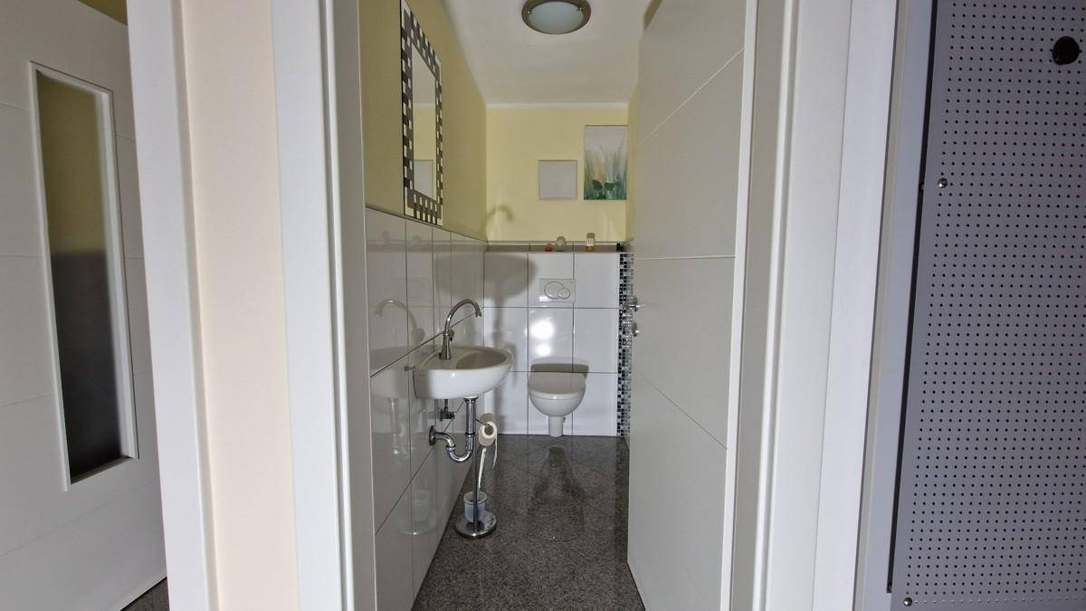 Helles Gäste-WC mit Waschbecken, Toilette und weißen Fliesen, einladend und funktional gestaltet.