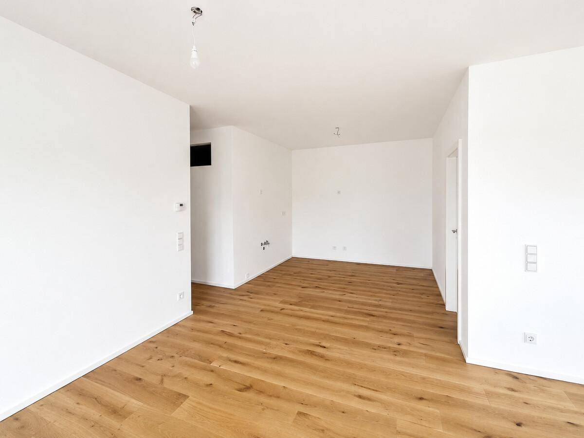 Geräumiger, leerer Wohnbereich mit hellem Eichenparkett und frisch gestrichenen Wänden.