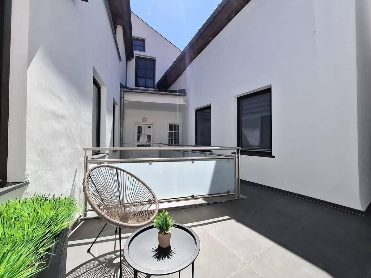 Sonniger Innenhof mit Terrasse, modernen Möbeln und hohen weißen Wänden, die Privatsphäre bieten.
