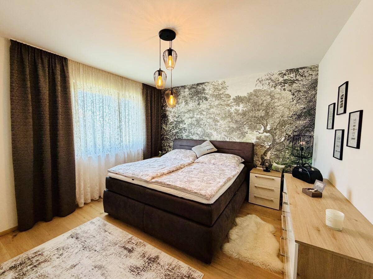 Schlafzimmer mit Doppelbett, Holzboden und dekorativer Waldtapete an einer Wand.