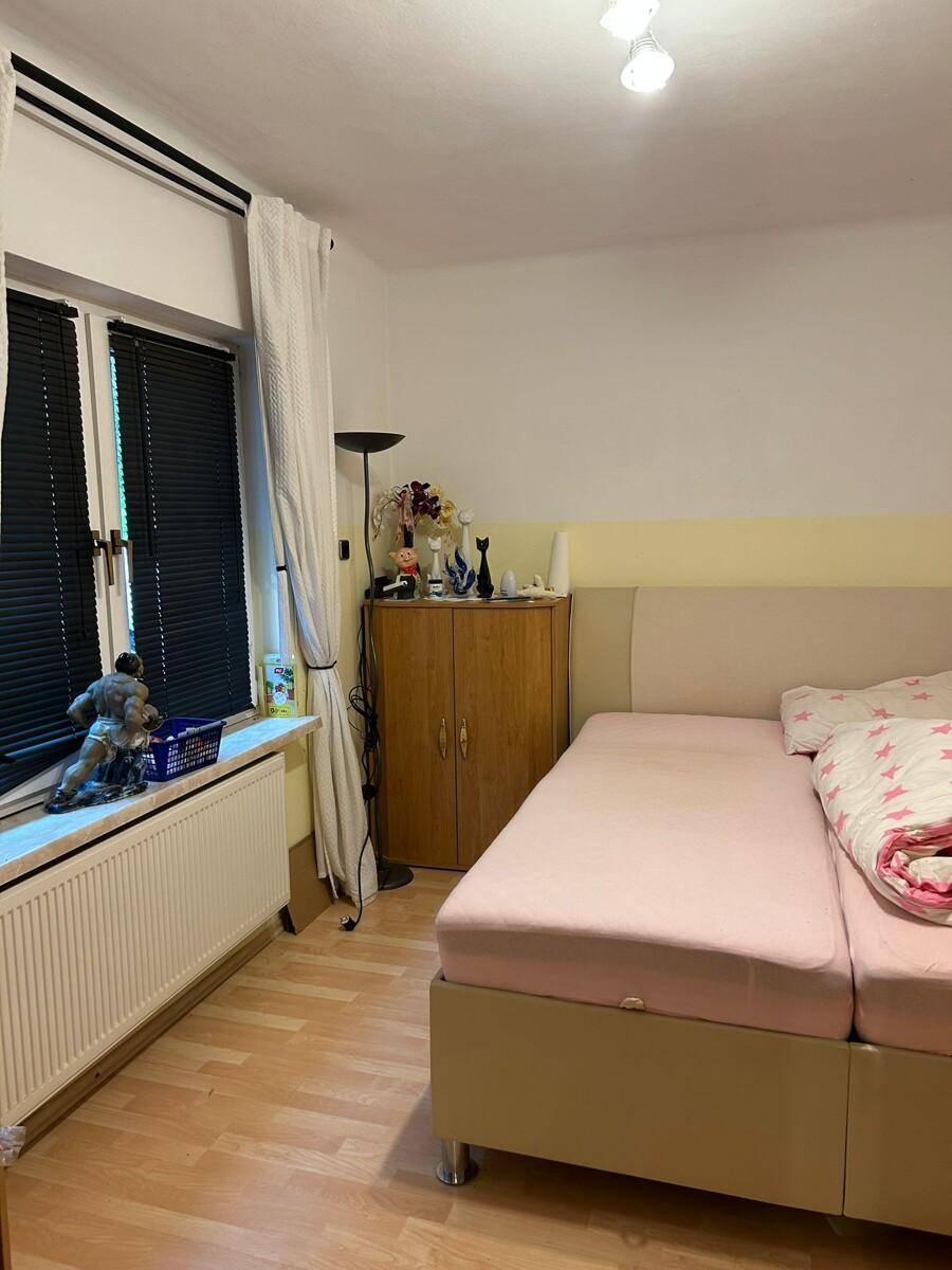 Schlafzimmer mit Doppelbett, Fenster und Heizkörper, einfach und funktional eingerichtet.