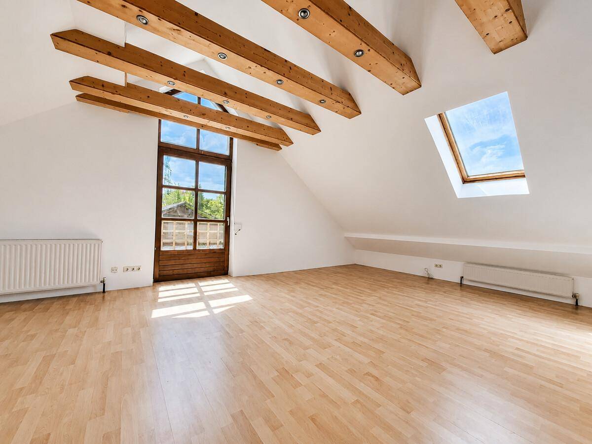 Dachbodenraum mit Holzbalken, Parkettboden, Dachfenster und viel Tageslicht.