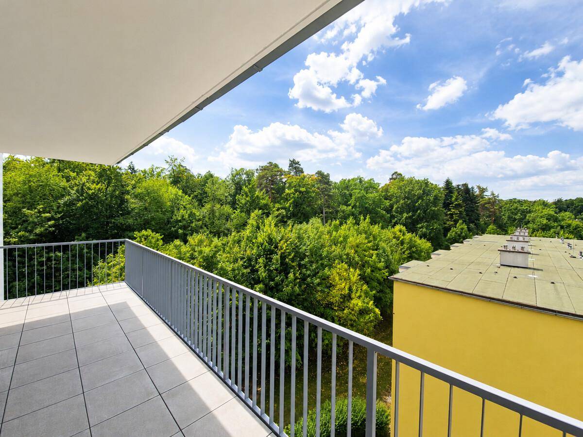 Geräumiger Balkon mit Fliesenboden und weitem Blick ins Grüne unter blauem Himmel.
