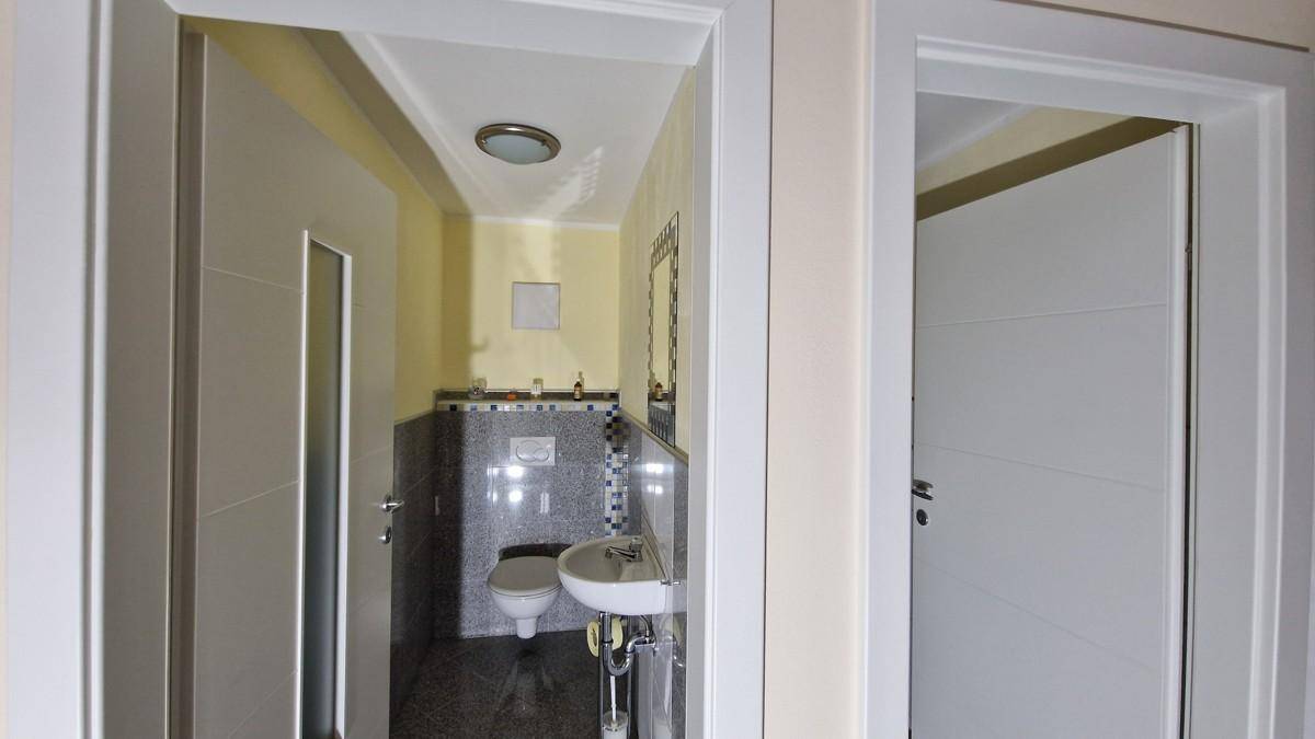 Kleines Gäste-WC mit Waschbecken, Toilette und dunklem Fliesenboden, praktisch und sauber.