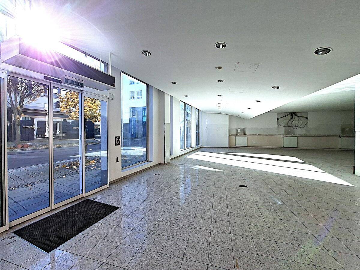 Großer, heller Gewerberaum im Erdgeschoss mit Fliesenboden und großen Schaufenstern zur Straße.