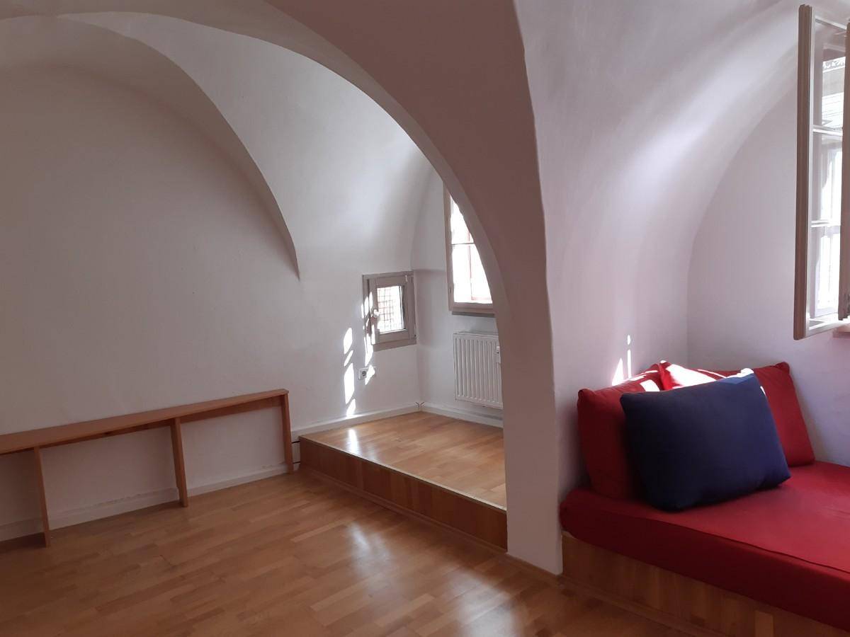 Geräumiger Wohnbereich mit Holzboden, Gewölbedecken und einer erhöhten Plattform mit Fenster.