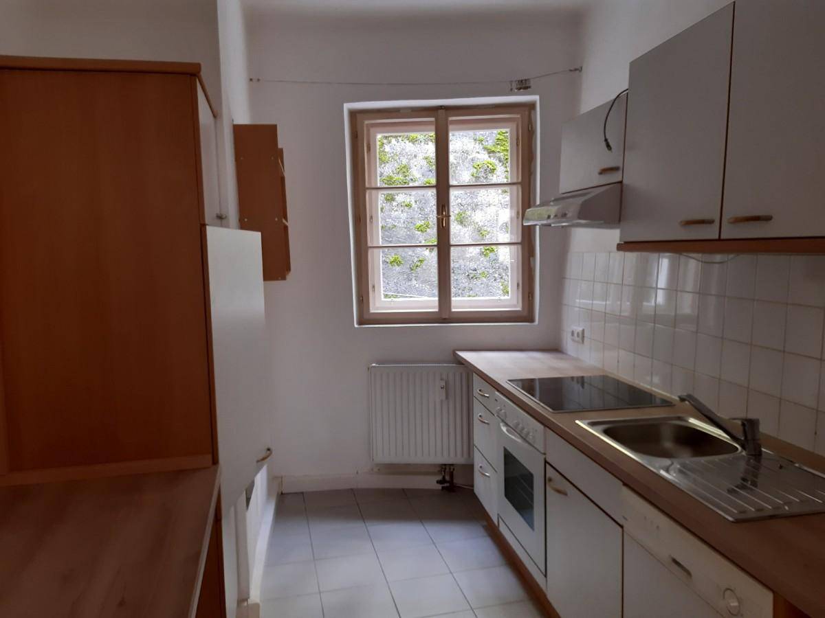 Funktionale Küche mit weißen Schränken, Holzarbeitsplatte, Spüle und Fenster mit Blick ins Grüne.