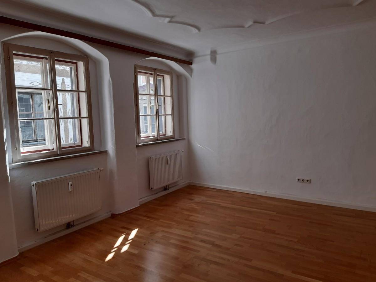 Heller, leerer Raum mit Holzboden, zwei Fenstern und dekorativer Decke in einem Altbau.