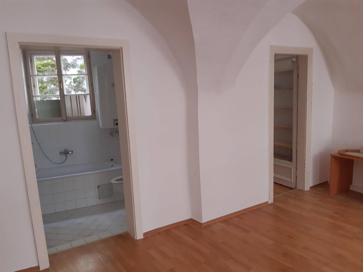 Heller Flur mit Holzboden und Gewölbedecken, der zu einem Badezimmer mit Badewanne führt.