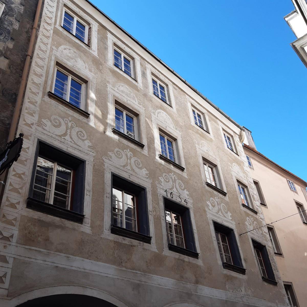 Historische Gebäudefassade mit dekorativen Malereien und vielen Fenstern unter blauem Himmel.