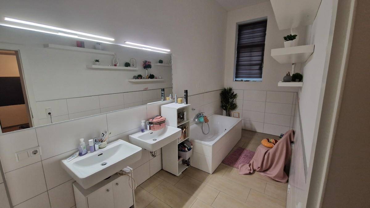Modernes Badezimmer mit Doppelwaschbecken, Badewanne und Fenster, hell gefliest.