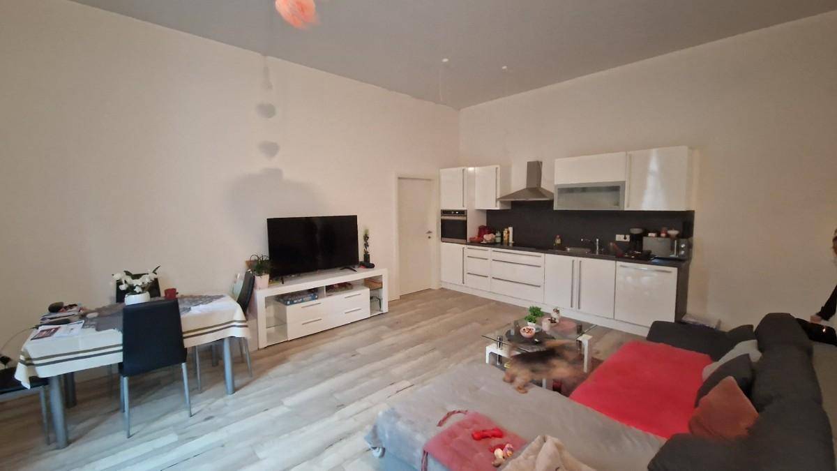 Offener Wohn-Essbereich mit moderner weißer Einbauküche und hellem Laminatboden.