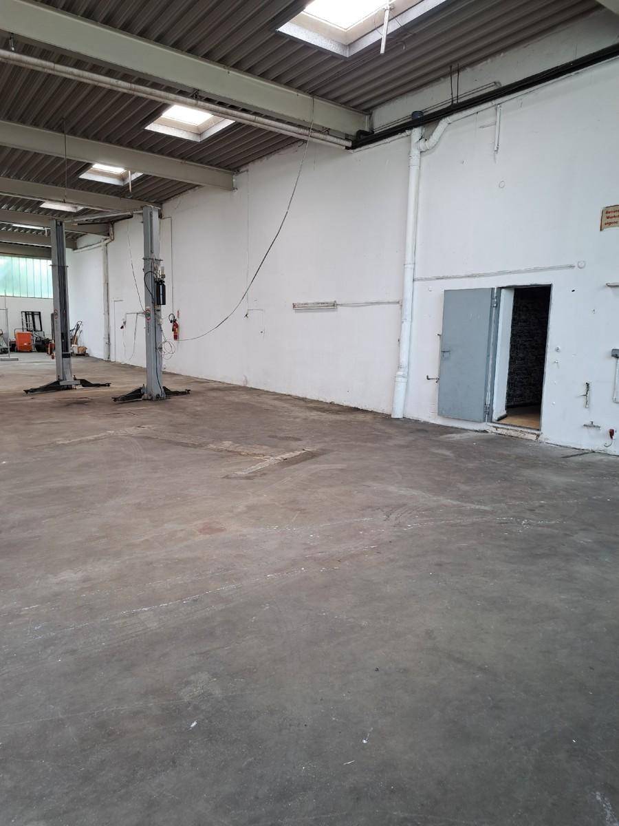 Blick in eine große Werkstatthalle mit Betonboden, hohen Wänden und einer einfachen Tür.