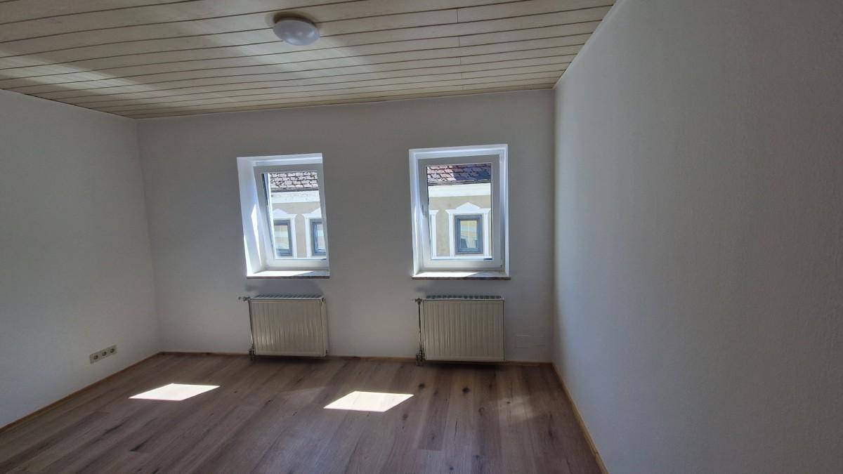 Freundliches Zimmer mit zwei Fenstern, Holzboden und Holzdecke, gut geeignet als Schlafzimmer.