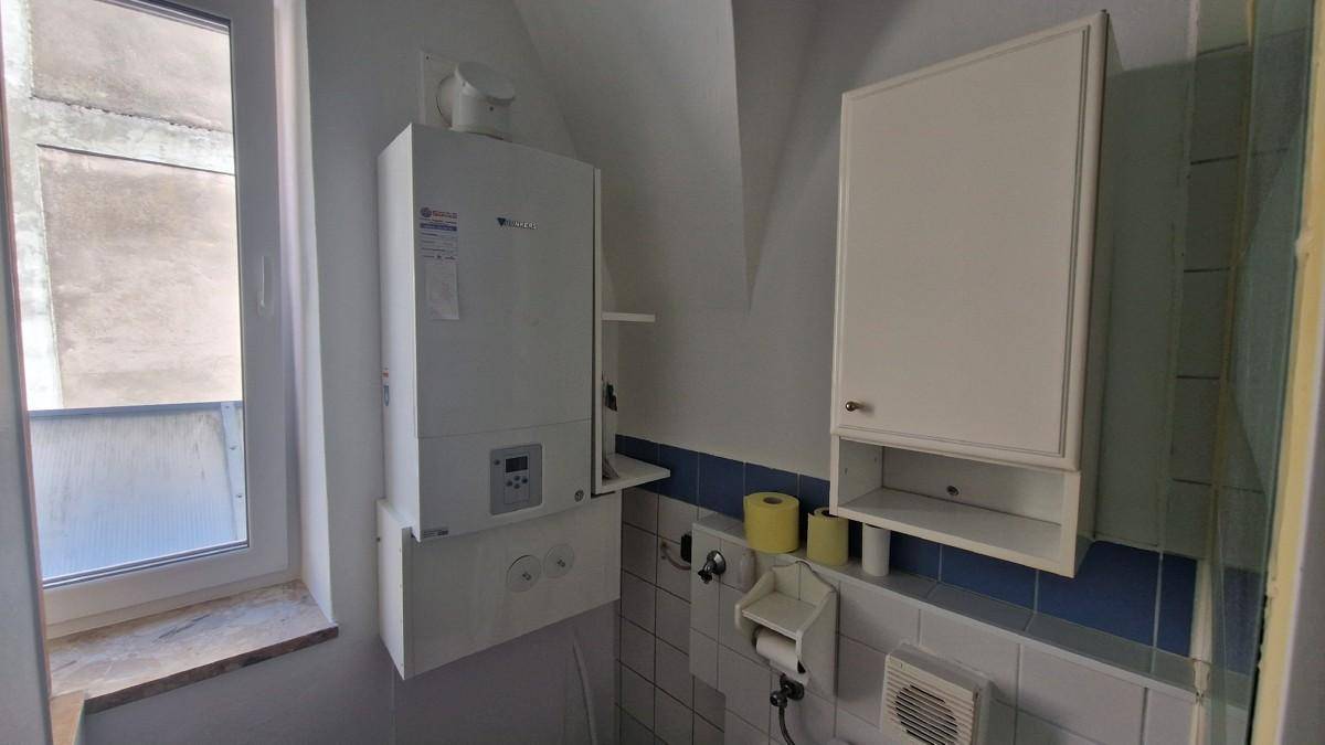 Kleiner Raum mit Fenster, Wandheizkessel und einem Hängeschrank über blau-weißen Fliesen.