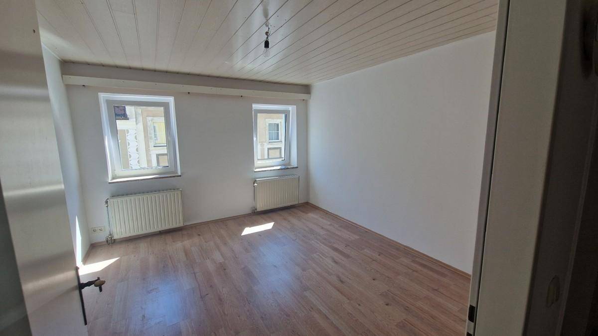 Heller Raum mit zwei Fenstern, Heizkörpern und Holzboden, ideal als Wohn- oder Schlafzimmer.