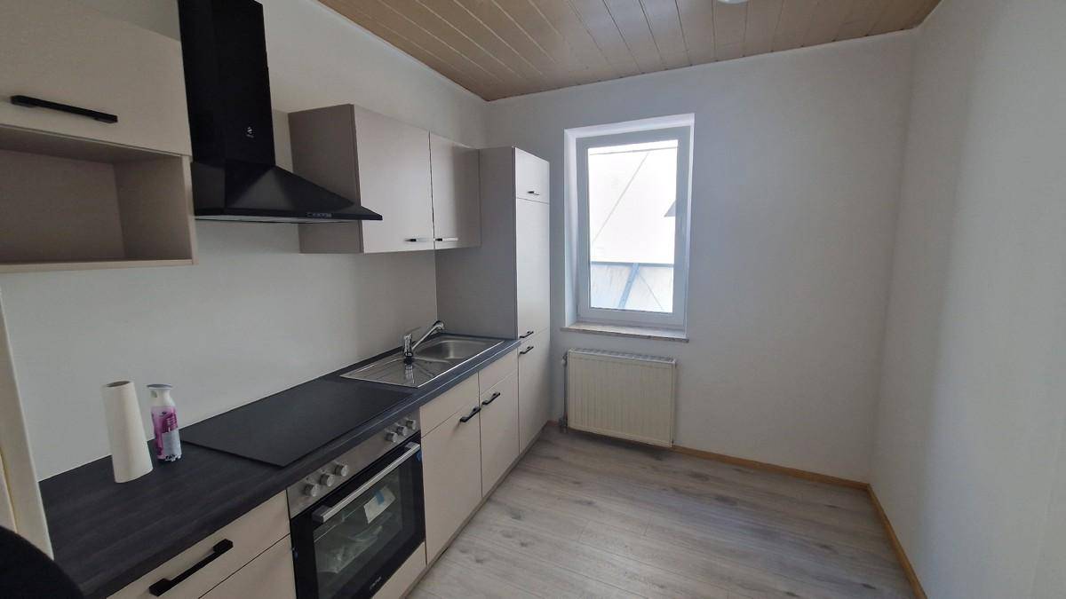 Moderne Küche mit hellen Schränken, schwarzer Arbeitsplatte, Spüle und integriertem Backofen.