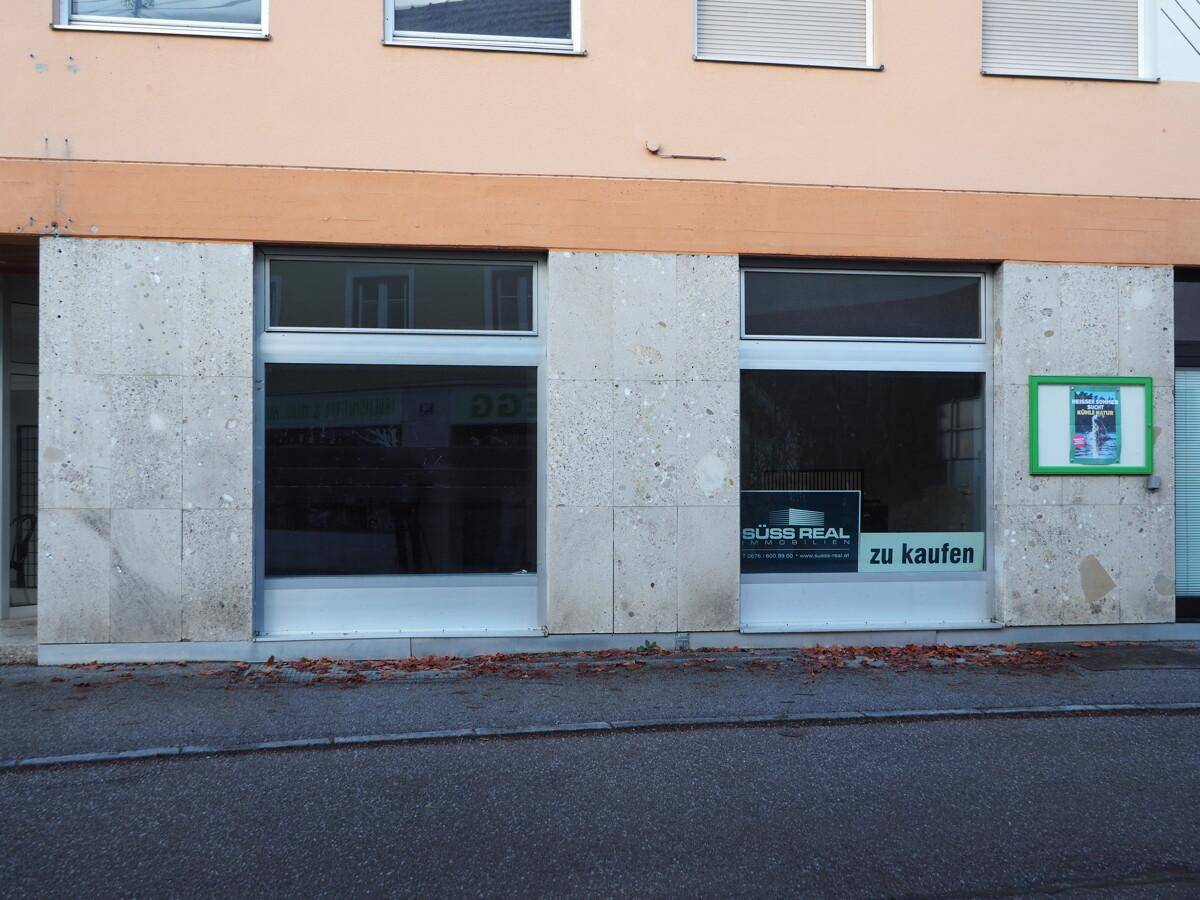 Gebäudefassade mit zwei großen Schaufenstern und einer Verkaufsanzeige.