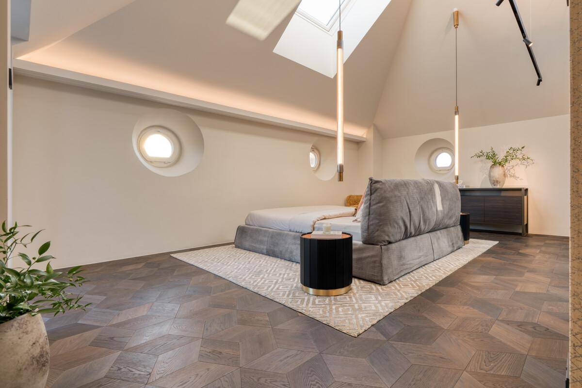 Geräumiges Schlafzimmer mit schrägem Dach, runden Fenstern und elegantem Holzboden.