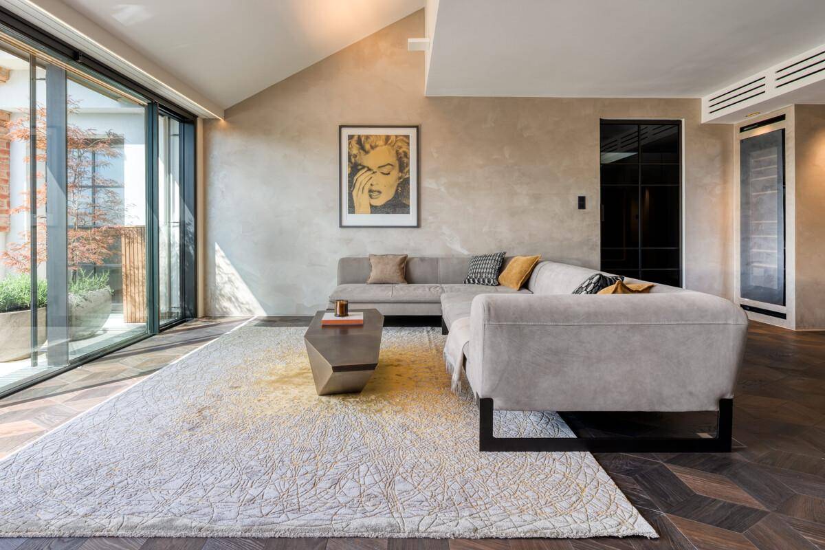 Helles Wohnzimmer mit großen Glasfronten, modernem Sofa und dunklem Fischgrätparkett.