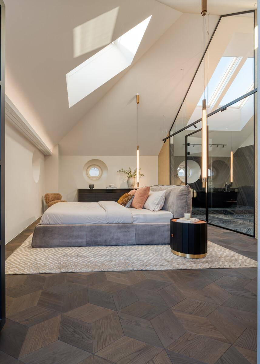 Helles Schlafzimmer im Dachgeschoss mit Dachfenstern, modernem Bett und Holzboden.