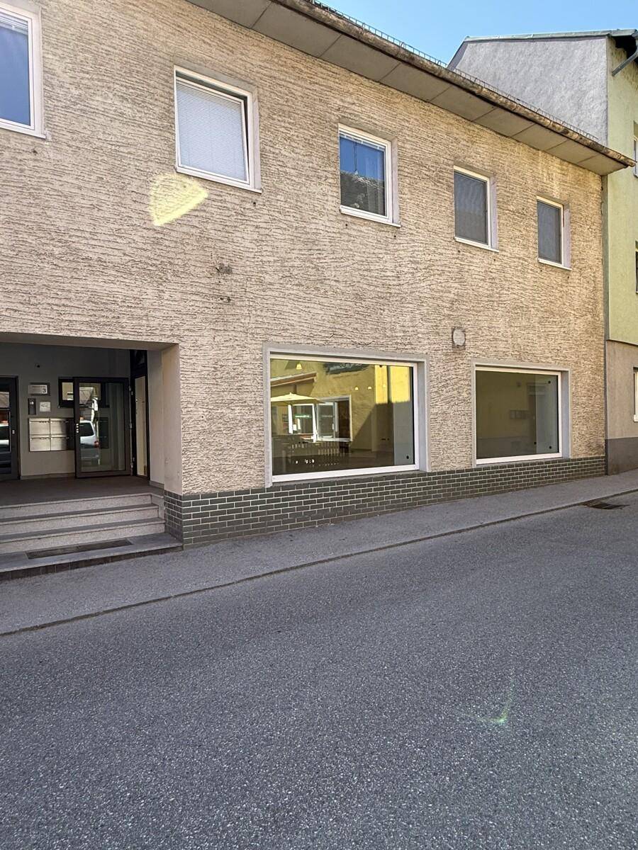 Ansicht der Gebäudefassade mit Eingangsbereich und großen Fenstern zur Straße hin.