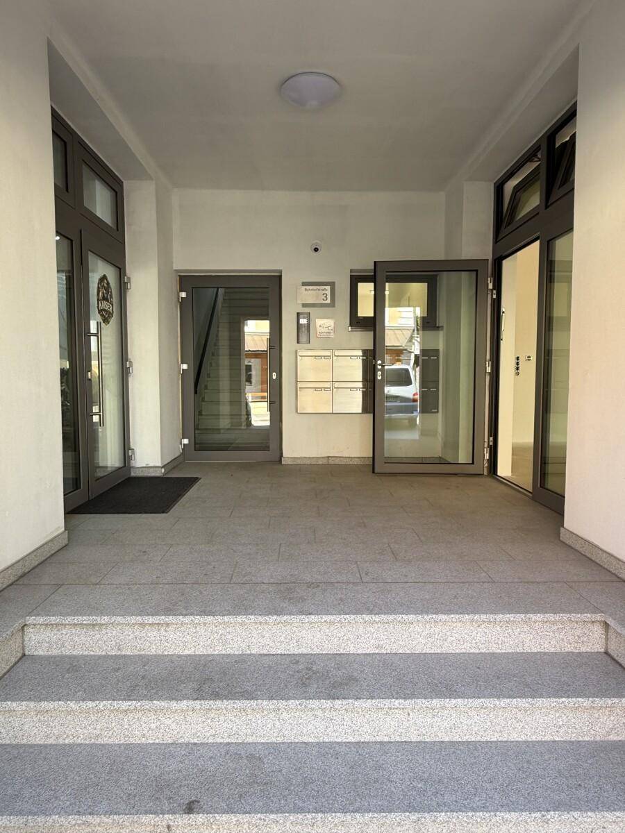 Heller Eingangsbereich mit Treppen, Fliesenboden, mehreren Türen und Briefkästen.