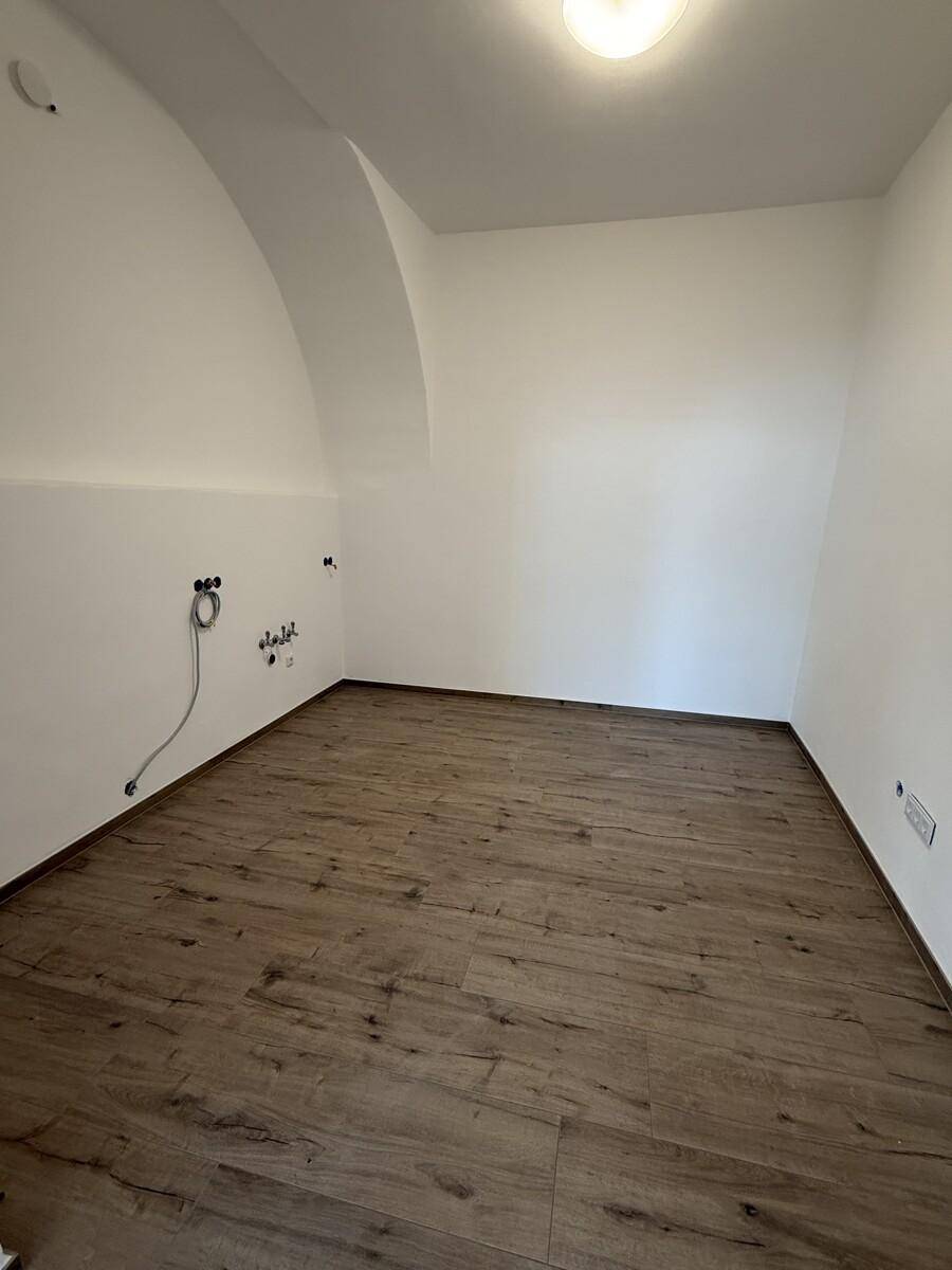 Leerer Raum mit weiß gestrichenen Wänden, gewölbter Decke und neuem Laminatboden, vorbereitet für Installationen.