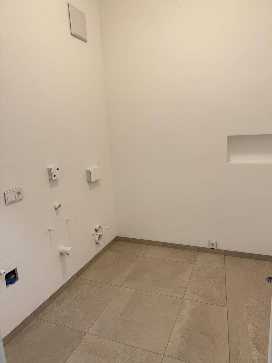 Raum mit Fliesenboden und weißen Wänden, vorbereitet für Badezimmerinstallationen mit zahlreichen Anschlüssen.