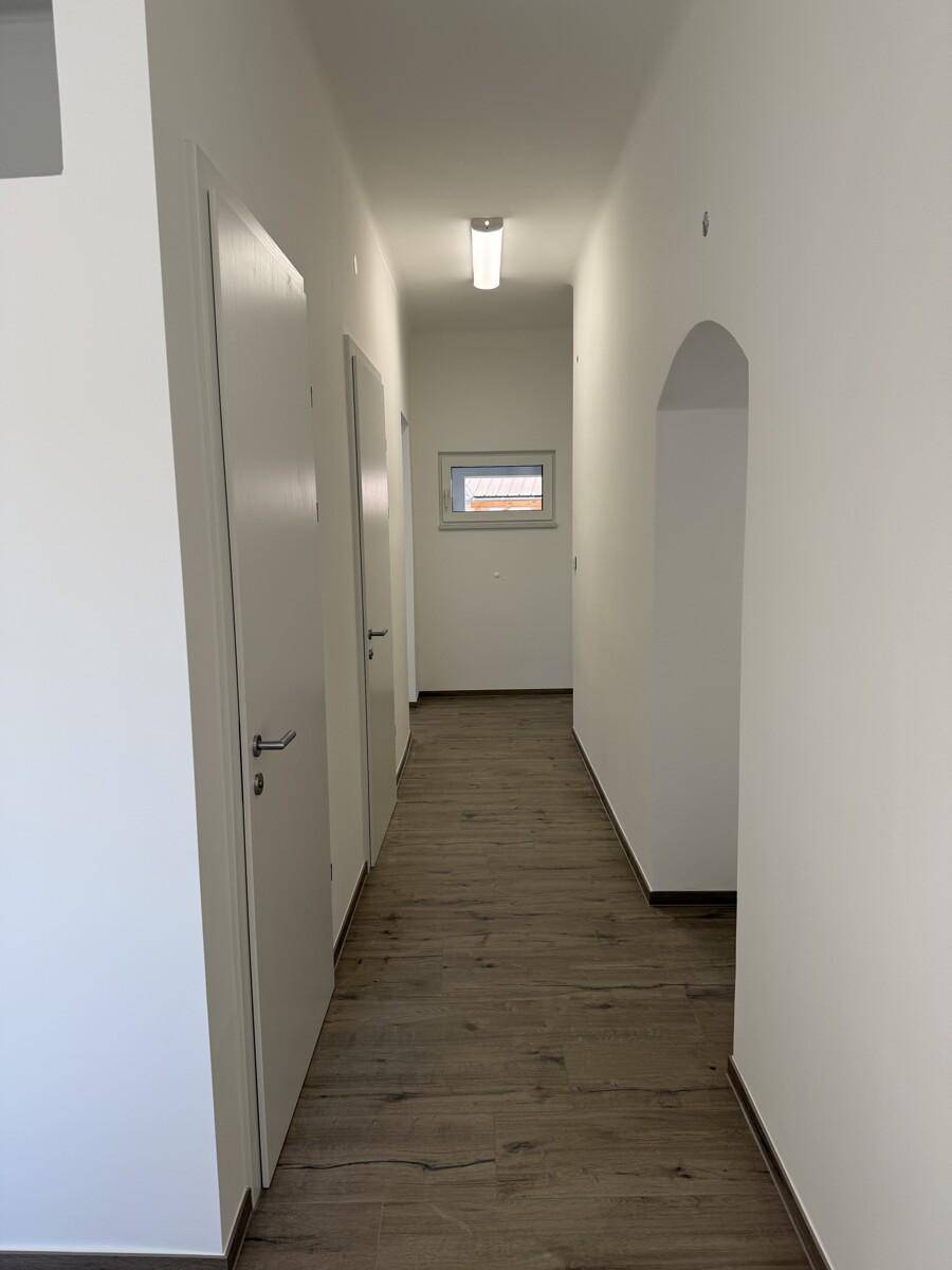 Langer, heller Flur mit mehreren weißen Türen, Laminatboden und einem kleinen Fenster am Ende.