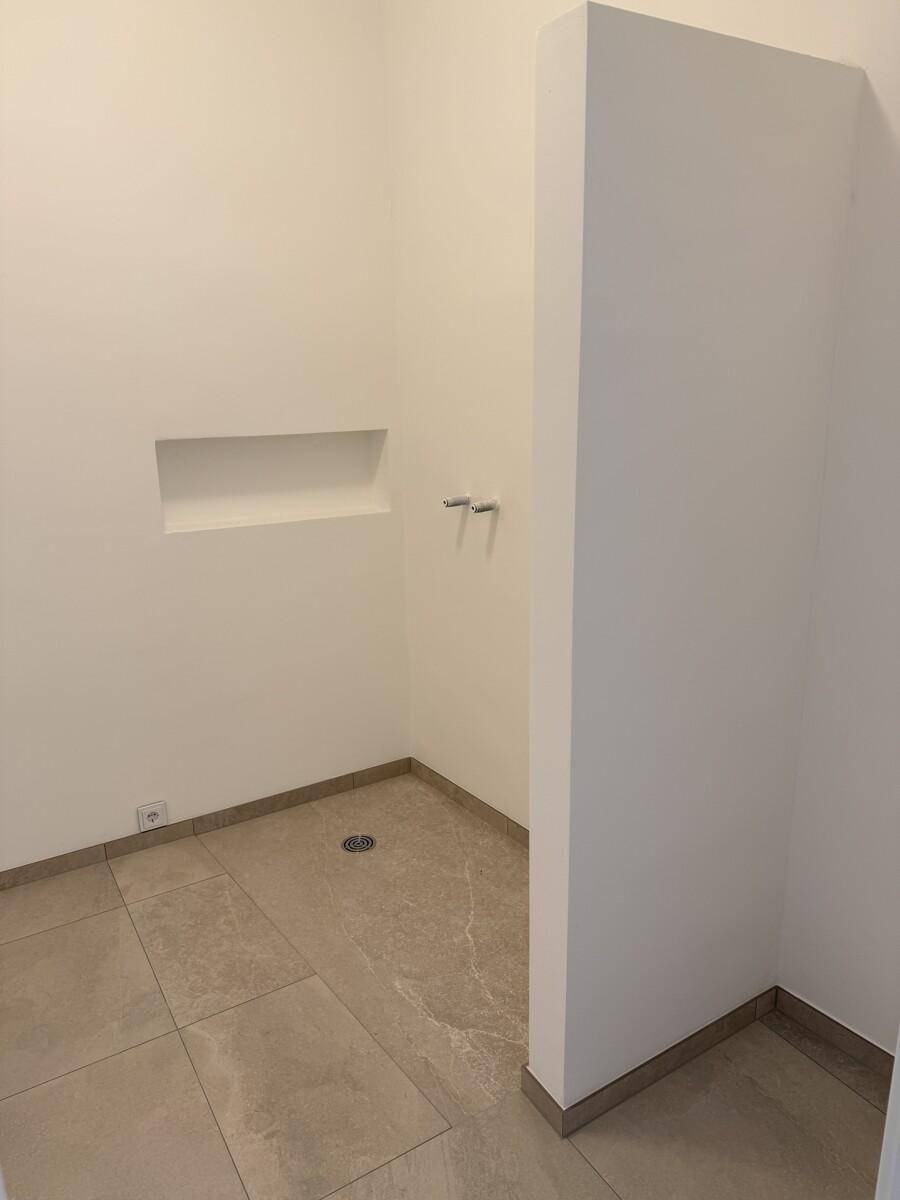 Kleiner Raum mit Fliesenboden und Wandnische, vorbereitet für eine Dusche mit sichtbaren Anschlüssen.