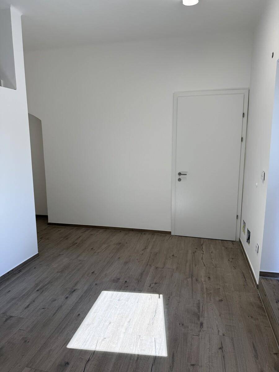 Heller, leerer Raum mit Laminatboden, weißen Wänden und einer modernen weißen Tür.