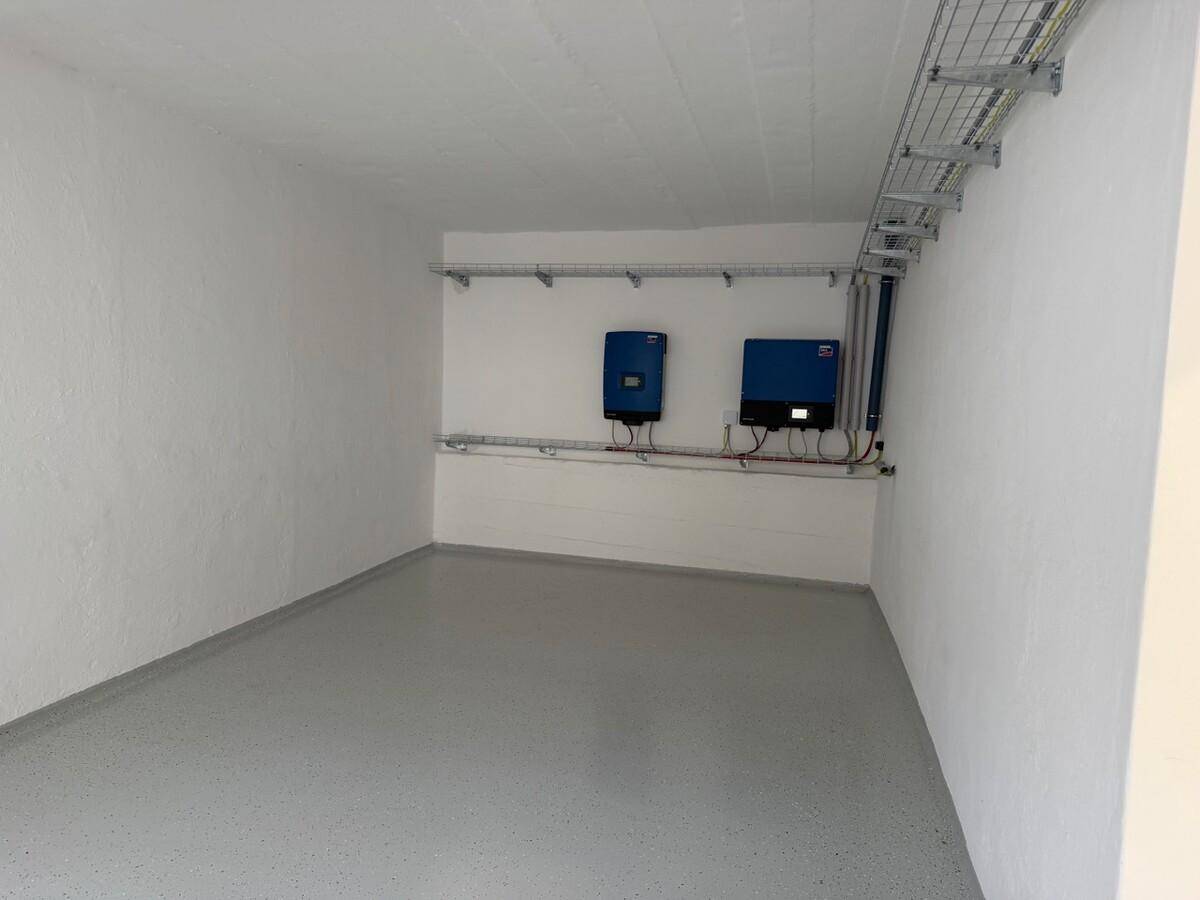Technikraum mit weißen Wänden, grauem Boden und an der Wand montierten Wechselrichtern für Solaranlagen.