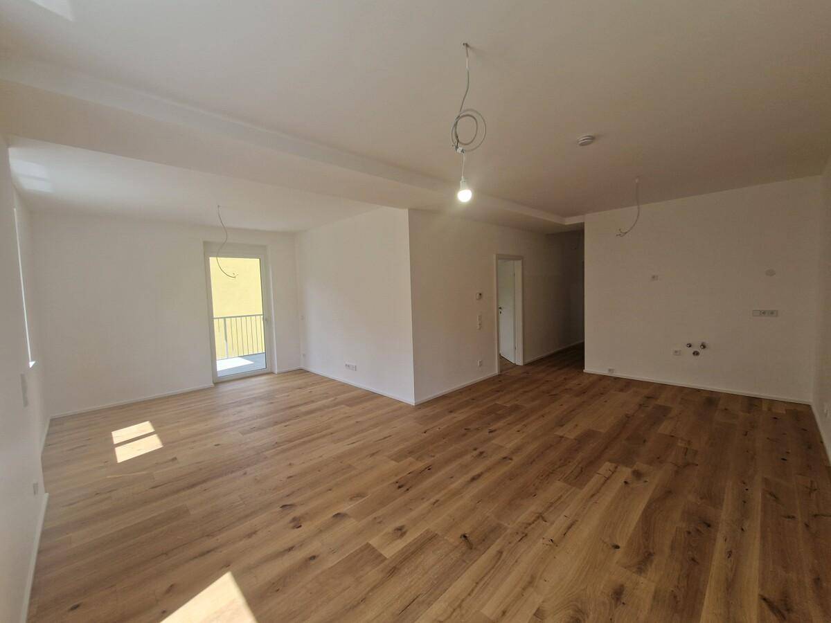 Helles Wohnzimmer mit neuem Holzplankenboden und Zugang zu einem Balkon, bereit zum Einzug.