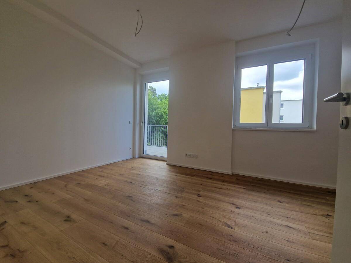 Helles Schlafzimmer mit Holzplankenboden, Fenster und Balkonzugang, ideal für eine ruhige Atmosphäre.