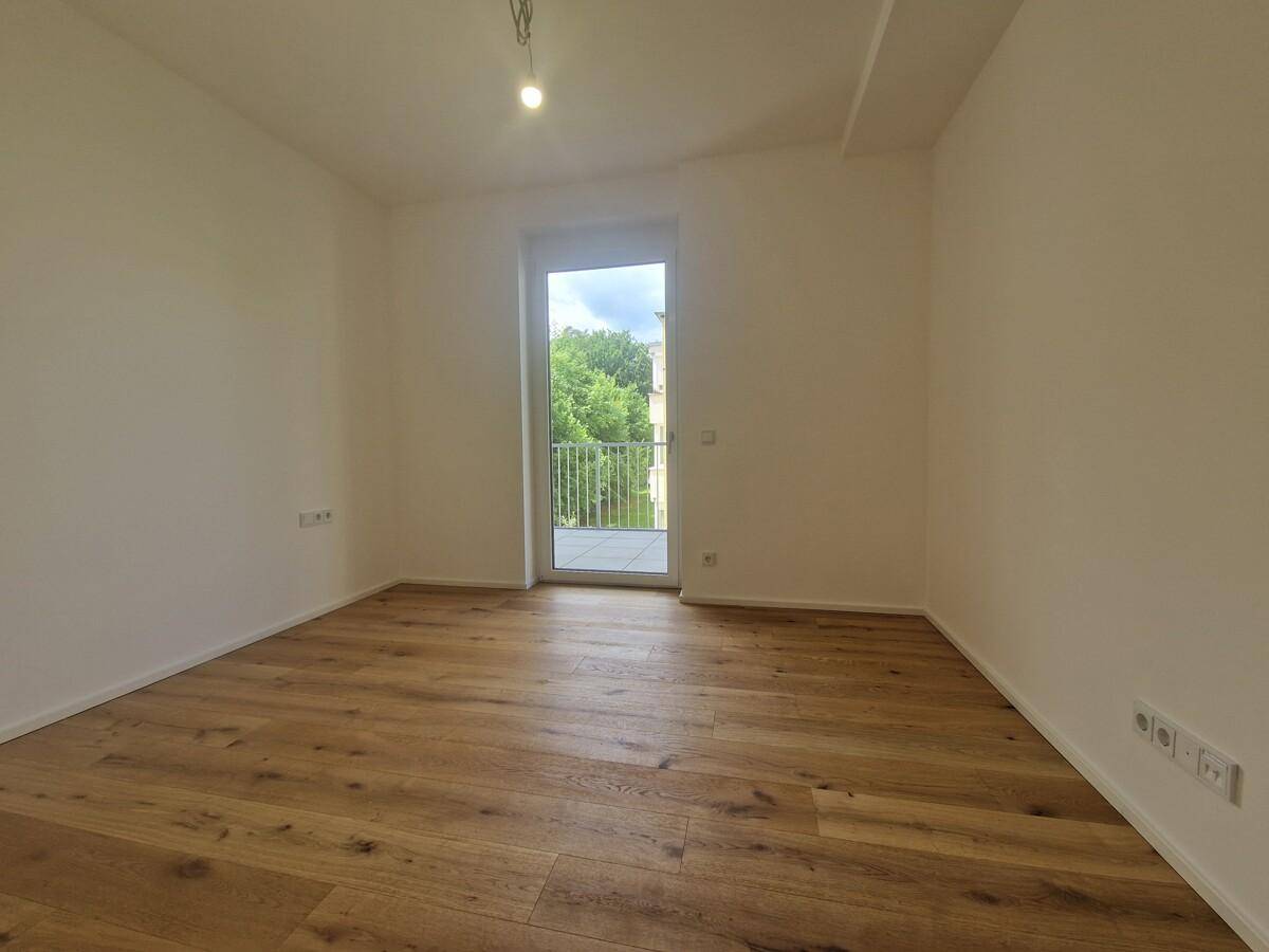 Schlafzimmer mit hellem Holzplankenboden und direktem Zugang zum Balkon, bietet viel Tageslicht.