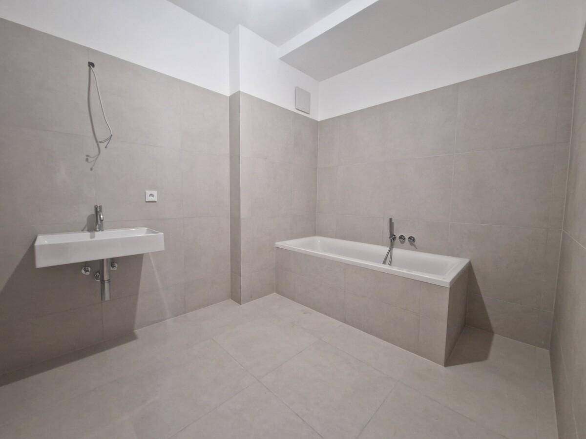 Geräumiges Badezimmer im Rohbau mit grauen Fliesen, Badewanne und wandhängendem Waschbecken.
