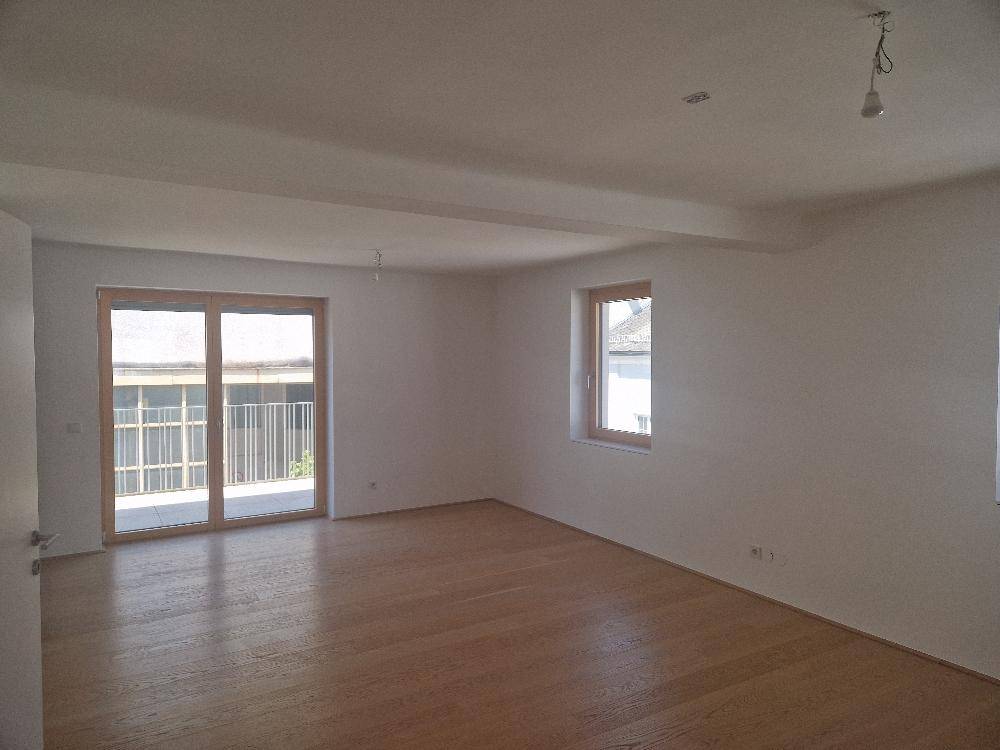 Heller Wohnraum mit Holzboden und Zugang zu einem Balkon oder einer Terrasse.
