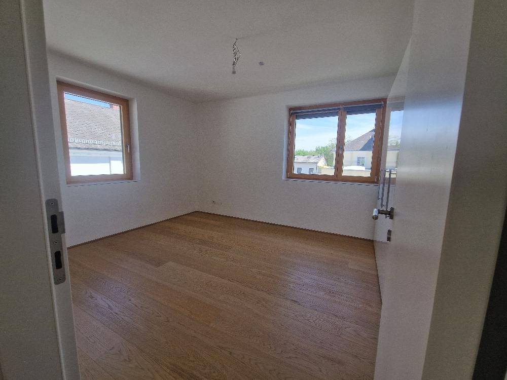 Helles Schlafzimmer mit Holzboden und zwei Fenstern für viel Tageslicht.