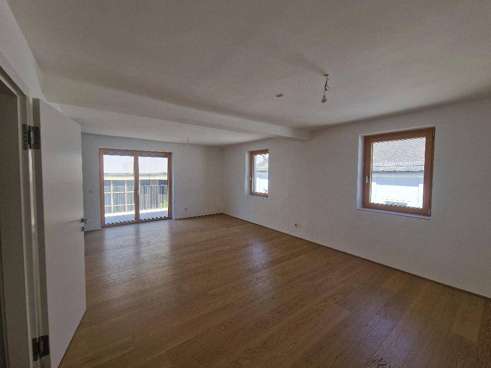 Heller Wohnraum mit Holzboden und Zugang zu einem Balkon oder einer Terrasse.