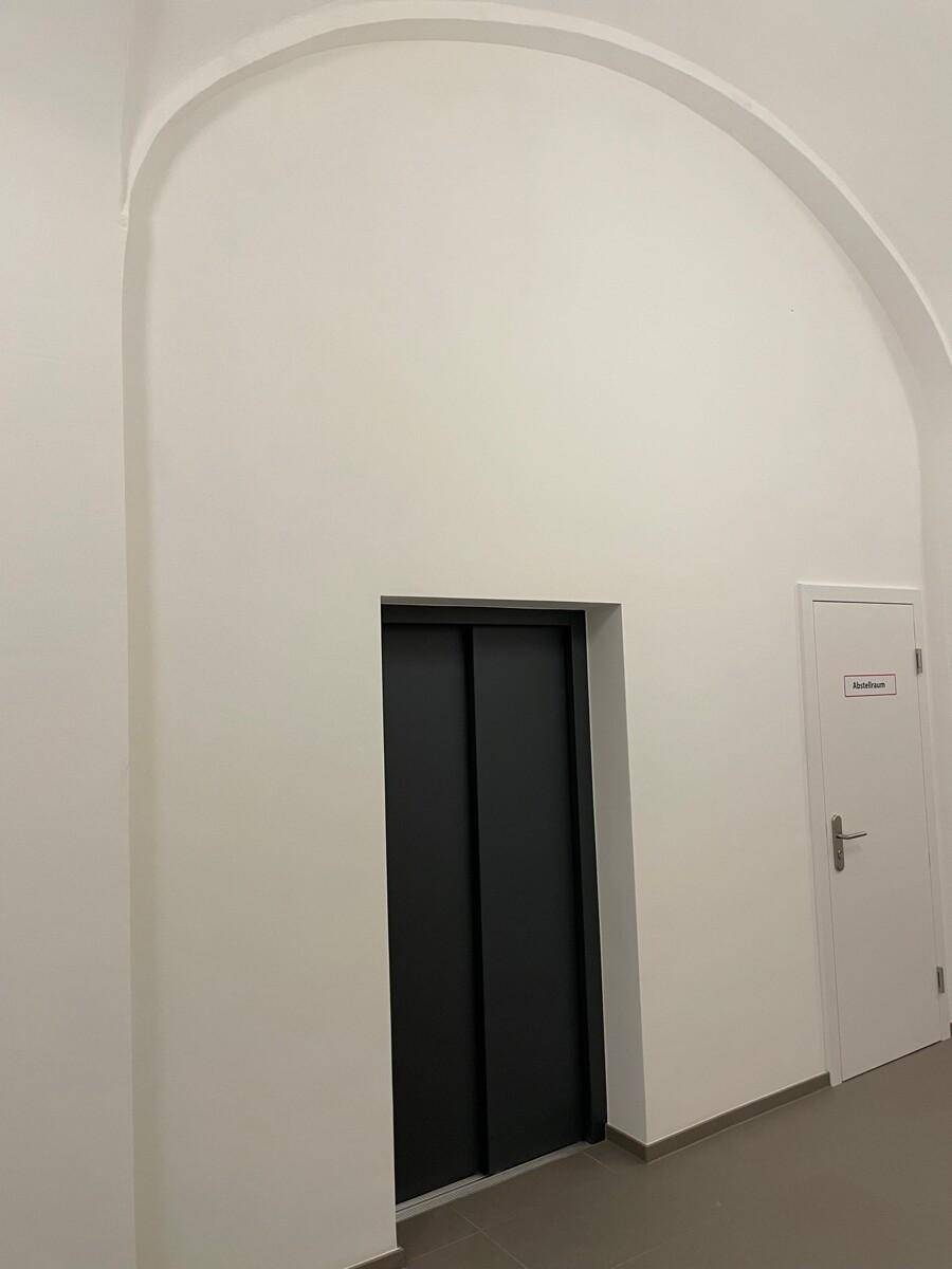 Heller Flur mit modernem Aufzug und weiß gestrichenen Wänden.