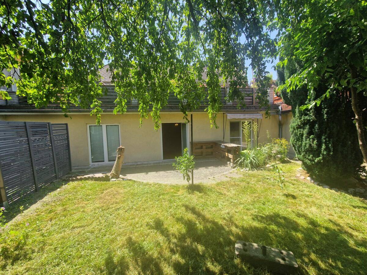 Rückseite des Hauses mit einer gepflasterten Terrasse und einem grünen Gartenbereich.