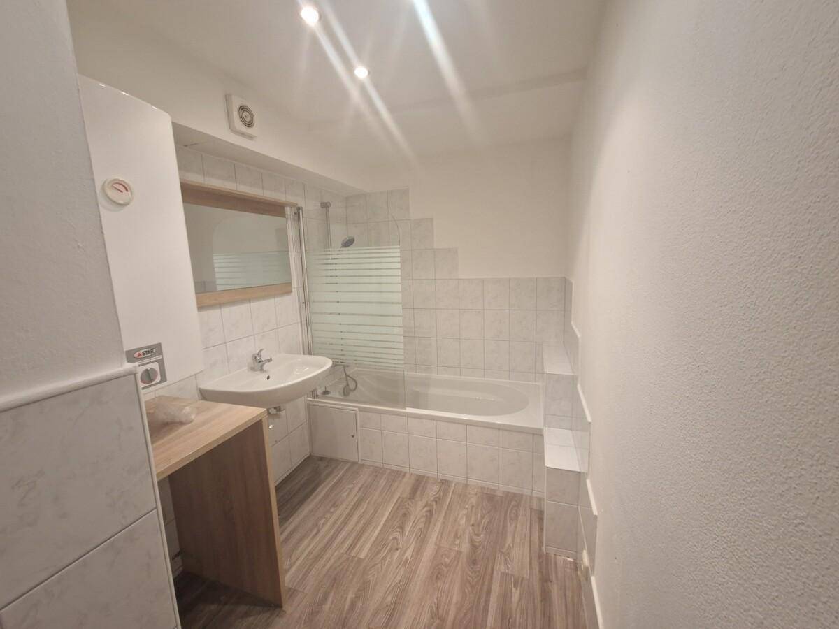Helles Badezimmer mit Badewanne, Waschbecken und Fliesenboden in einem funktionalen Design.
