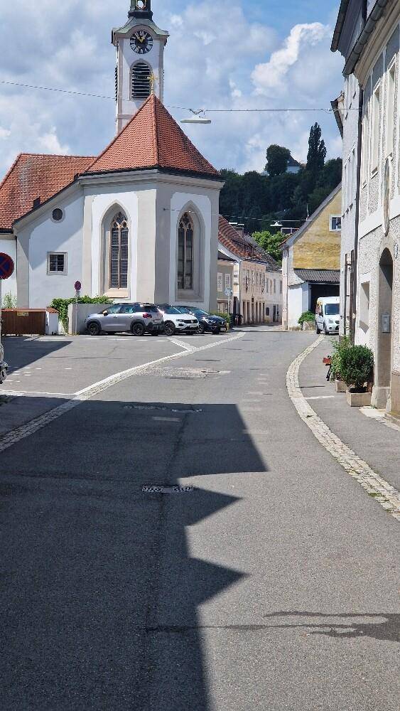 Eine ruhige Straße mit einer Kirche im Hintergrund und geparkten Autos an einem sonnigen Tag.