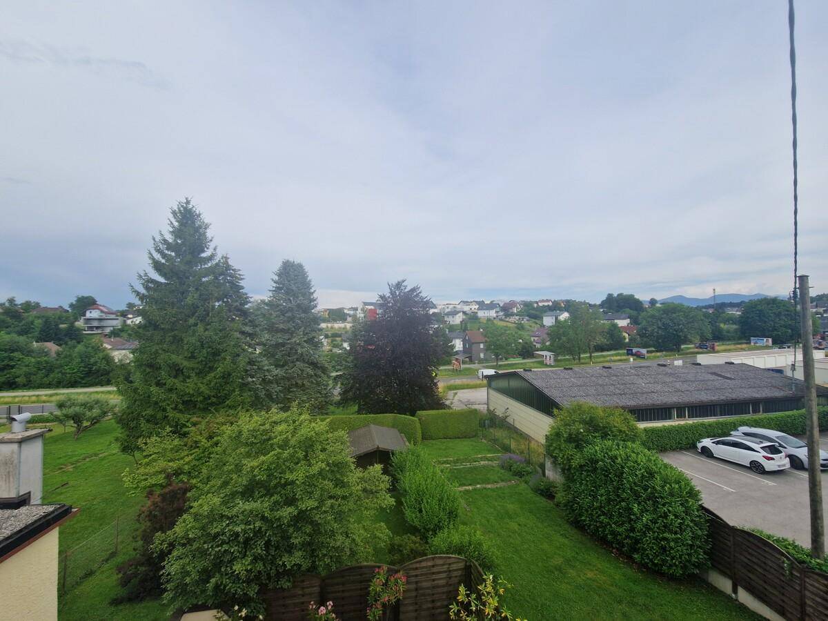 Weitläufiger Blick über die grüne Umgebung mit Häusern und Bäumen unter bewölktem Himmel.